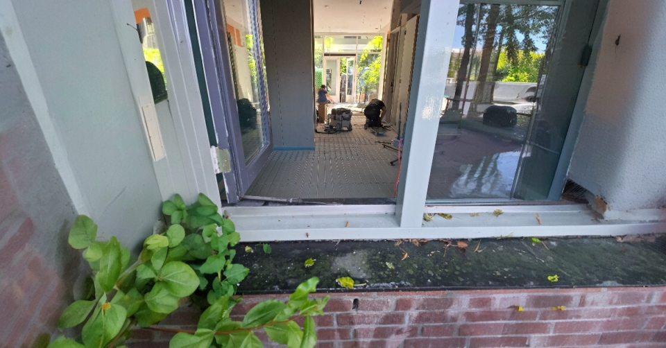 Vanuit buiten kijk je via het raam een woning binnen waar ze vloerverwarming leggen.