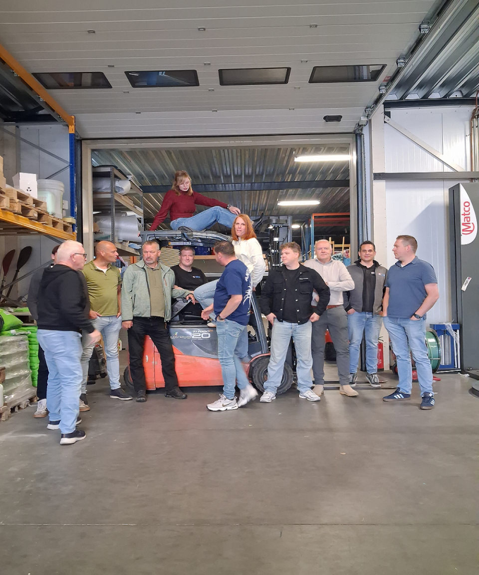 Groepsfoto van het Uniwarm-team in het magazijn, met collega&rsquo;s rondom een heftruck bij de overheaddeur.