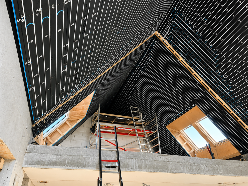 Uniwarm ISO-decke mit integrierten Fußbodenheizungsrohren, montiert an der Dachschräge eines Neubaus. Energieeffizientes System für Deckenheizung und -kühlung, ideal für nachhaltige Gebäude in Kombination mit einer Wärmepumpe.