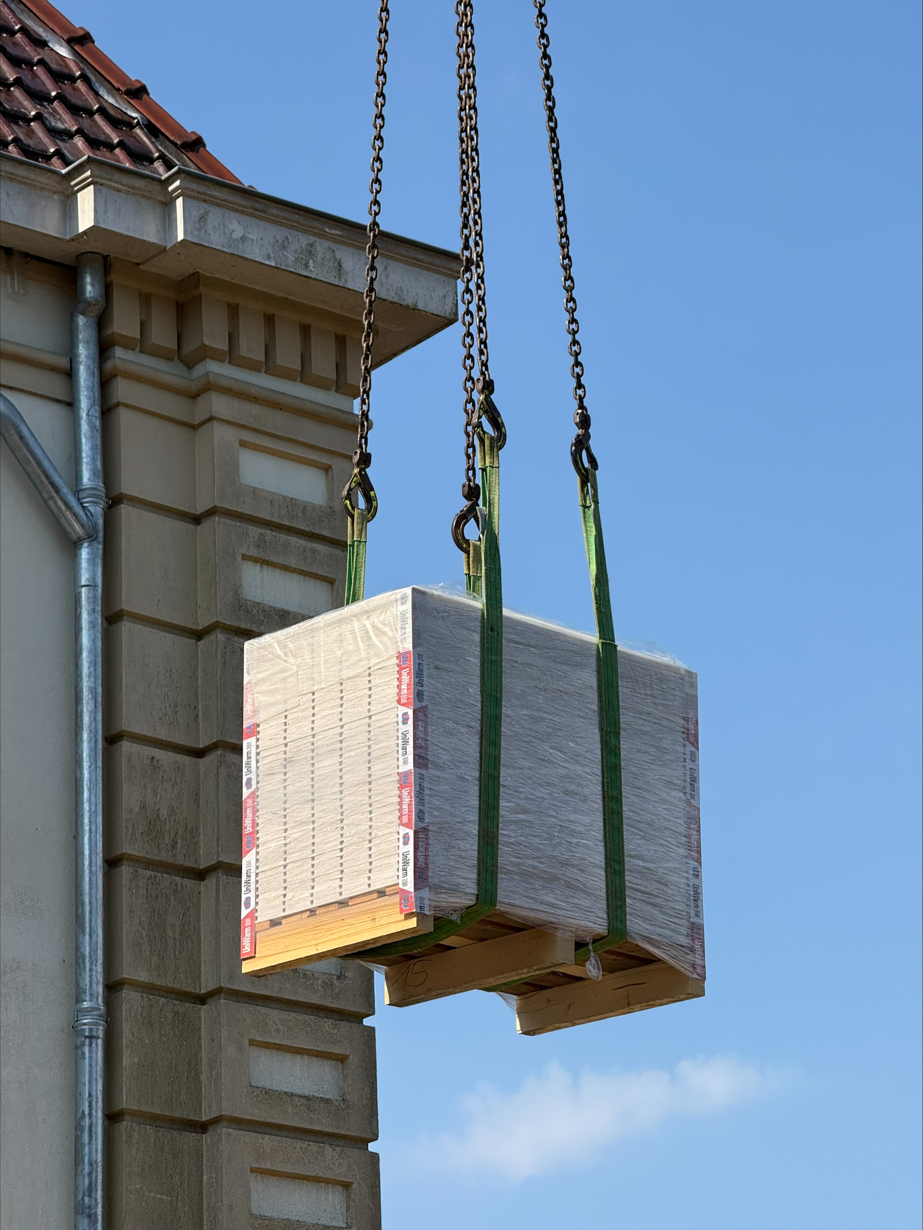 Pallet met Uniwarm droogbouwplaten wordt met een kraan naar de verdiepingsvloer gehesen tijdens de renovatie van een monumentaal klooster.