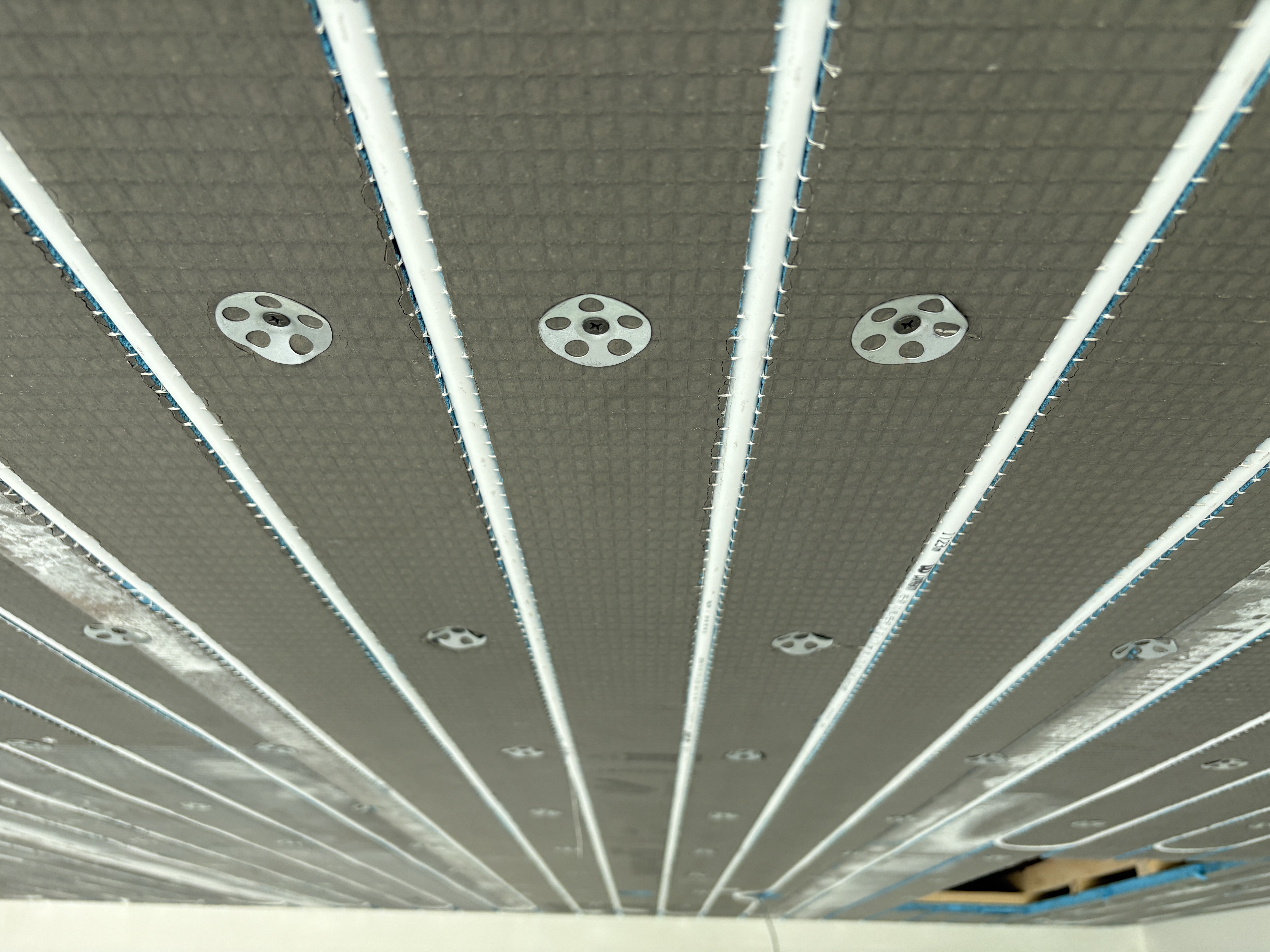 Koelplafond met strak geplaatste leidingen in isolatieplaten, bevestigd tegen het plafond.