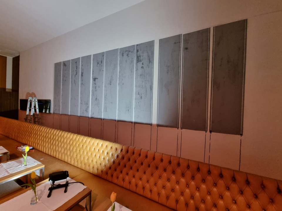 Eine Restaurantwand mit teilweise montierter Papierwandheizung, einer langen Lederbank und Tischen mit wei&szlig;en L&auml;ufern und Tulpen in Vasen.