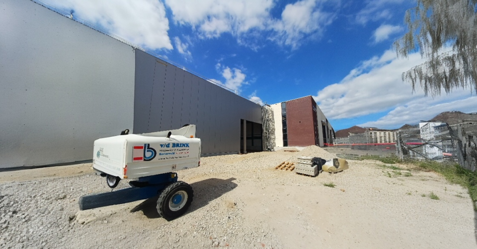 zijkant van een grote fabriekshal in aanbouw met op de voorgrond een machine op wielen.