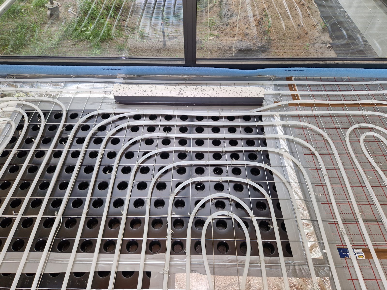 Detail eines UniWarm Fußbodenheizungssystems mit Lüftungsboden. Die Heizrohre sind präzise verlegt und gewährleisten eine optimale Wärmeverteilung sowie ein effizientes Heizsystem.