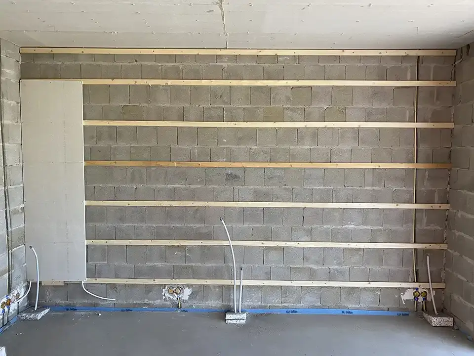 Steinmauer mit Holzraster, ein Wandmodul mit Leitung ist bereits an der Wand montiert